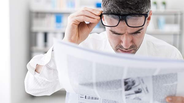 Un hombre sin gafas progresivas ocupacionales forzando la vista para leer el periódico