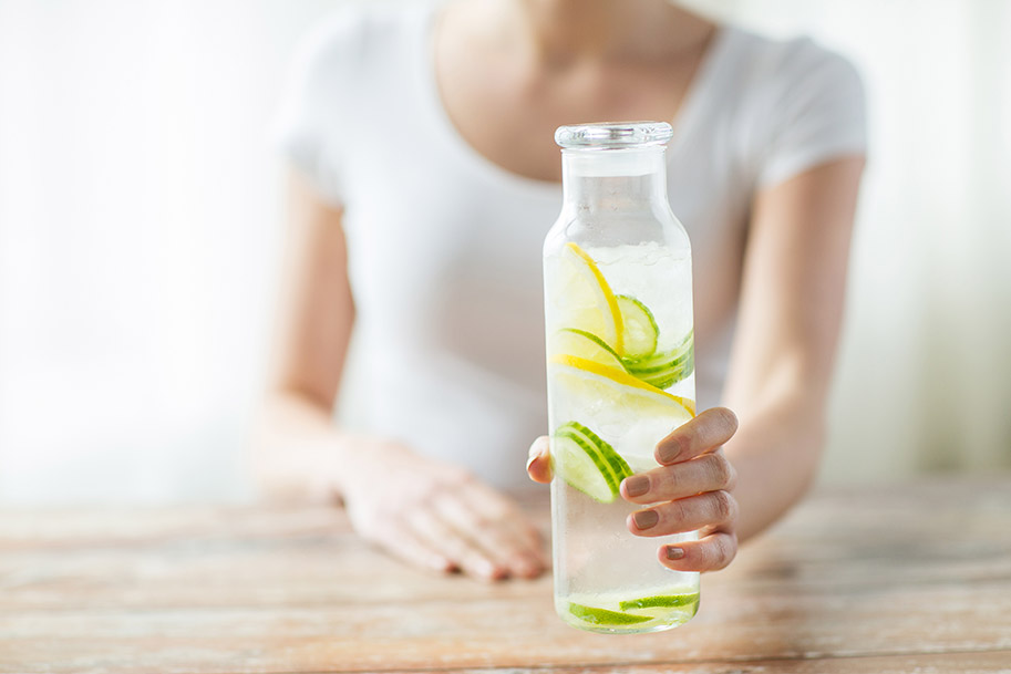 Cuerpo de mujer sosteniendo una botella de agua fría con rodajas de limón.