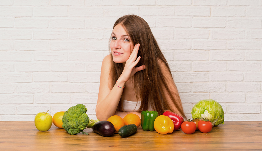 Chica con mano en oido escuchando y con alimentos sanos en la mesa