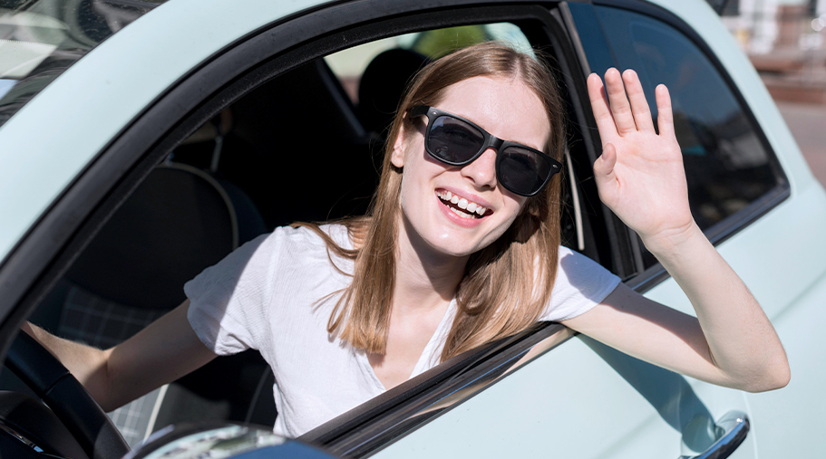 Chica en el coche saludando con gafas de sol