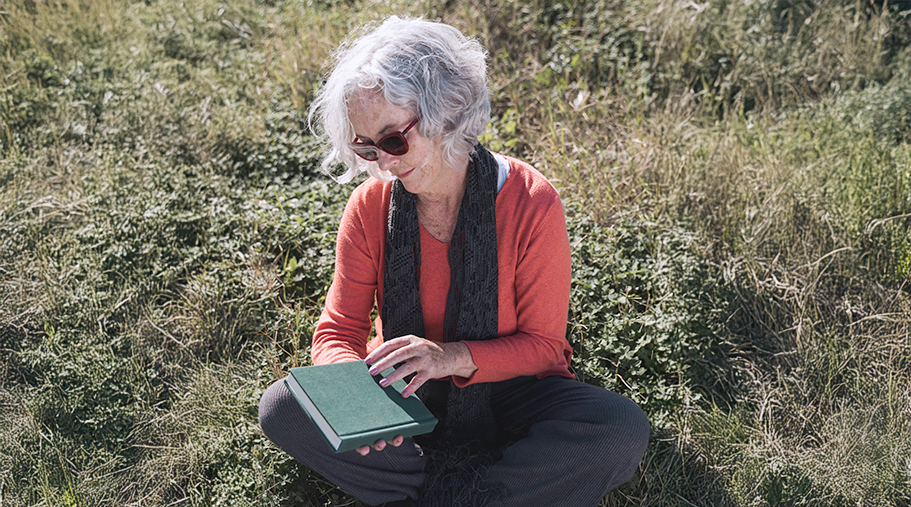Mujer madura leyendo con gafas de sol, sentada en el cesped