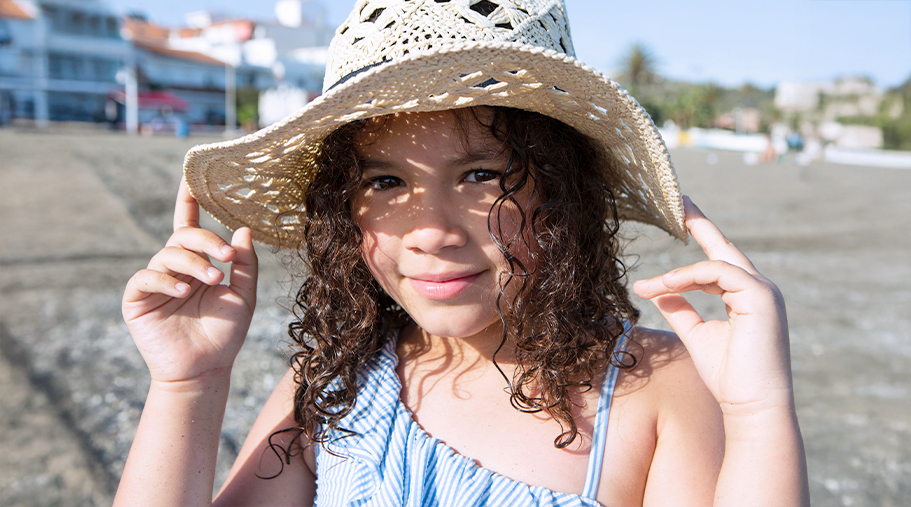 Niña en entorno playero con un sombrero que le da sombra en los ojos
