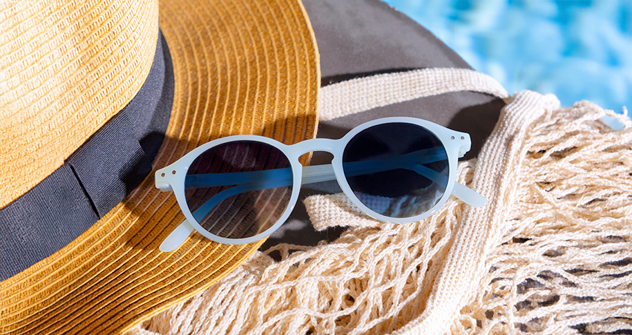 Gafas de sol junto a un sombrero, un pareo y una piscina.