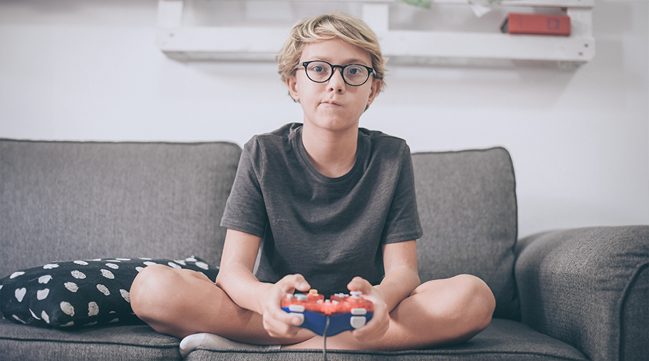 Niño jugando a vedeojuegos con cara de cansado.